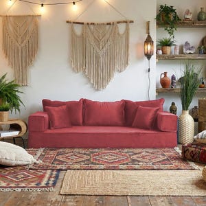 Peut inclure: Salon confortable avec un canapé rouge, des tapis à motifs et des plantes. Des tentures murales en macramé et une lampe suspendue ajoutent à l'esthétique bohème. La pièce est baignée de lumière naturelle et d'éléments décoratifs.