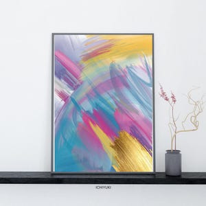 May include: Abstract art print with a vibrant mix of colors including blue, pink, yellow, and purple. A gold metallic brushstroke adds a touch of luxury. The artwork is framed in a gray border and displayed on a black shelf.