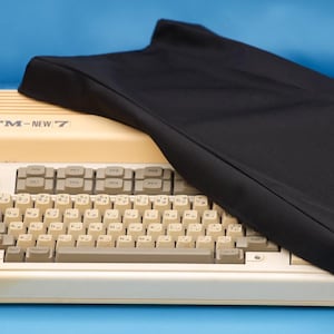 Op de afbeelding: Een beige FM-NEW 7 computertoetsenbord met een zwarte stoffen hoes die over het rechterbovengedeelte is gedrapeerd. Het toetsenbord heeft lichtgrijze toetsen met Japanse tekens en Engelse letters, en een geribbeld bovenpaneel met de tekst FM-NEW 7.