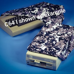 May include: Two vintage beige Commodore 64 computers and a 1541 disk drive are shown with covers. The covers are patterned with a digital camouflage design in shades of gray, black, and white. The text "C64 I shown as example" is visible.