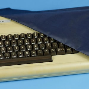 Könnte beinhalten: Ein Vintage-Commodore-Computer mit schwarzer Tastatur und marineblauem Bezug. Der Computer hat ein beiges Gehäuse und das Commodore-Logo ist sichtbar. Die Tastatur hat weiße Buchstaben auf den Tasten.