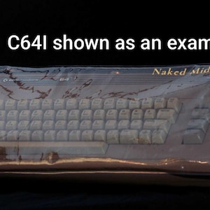 May include: A Commodore 64 computer encased in a clear plastic cover, featuring the text 'Naked Midnight' in gold lettering on the top right and 'C64I shown as an example' centered above the unit against a solid black background.