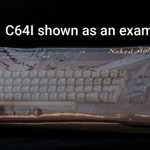 May include: A Commodore 64 computer encased in a clear plastic cover, featuring the text 'Naked Midnight' in gold lettering on the top right and 'C64I shown as an example' centered above the unit against a solid black background.