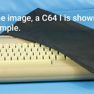 Peut inclure: Un ordinateur Commodore 64 beige avec un clavier complet et une housse noire. Le texte "In the image, a C64 I is shown as an example." est visible. L'ordinateur est sur une surface bleue.
