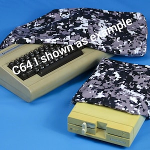 May include: Tan Commodore 64 computer with a black keyboard, covered by a digital camouflage cover. The cover is gray, black, and white. The text "C64 I shown as example" is visible on the computer.