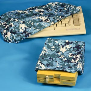 May include: A computer keyboard and a computer tower are covered with blue and white digital camouflage fabric covers. The keyboard is beige, and the tower is yellow. The background is a solid blue.