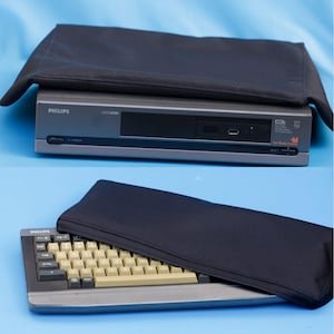 Könnte beinhalten: Ein grauer Philips NMS 8250 Computer mit schwarzer Stoffabdeckung, ausgestattet mit Ein-/Ausschalter, Diskettenlaufwerk und New Media Systems Branding. Darunter befindet sich eine graue Computertastatur mit beigen Tasten und schwarzer Hülle.