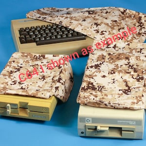 May include: Tan and brown camouflage covers for a Commodore 64 computer and two 1541 disk drives. The computer and drives are beige and yellow. The text "C641 shown as example" is visible.