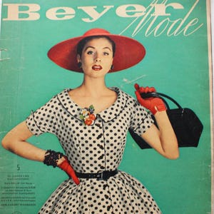 May include: A vintage Beyer Mode magazine cover featuring a person wearing a white dress with black polka dots, a red hat, and red gloves. The person holds a black handbag and wears a floral brooch. The background is teal with the text Beyer Mode.