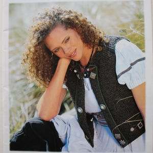 May include: A magazine cover featuring a woman wearing a dark green vest with silver buttons and trim. The cover has the word "Inspiration" in a cursive font, with text below that reads "Strickanleitungen" and "Landhausmode und Trachten für die ganze Familie."