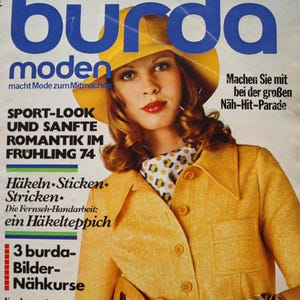 Può includere: Una copertina di rivista vintage Burda Moden del febbraio 1974 con una persona che indossa una giacca gialla, un cappello giallo abbinato e una sciarpa fantasia. La copertina include testo come Sport-Look und sanfte Romantik im Frühling 74.