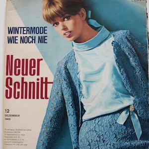 May include: A vintage magazine cover showing a woman in a light blue lace suit and top. The cover features the text "WINTERMODE WIE NOCH NIE" and "Neuer Schnitt" in red. The magazine is dated December 1965.
