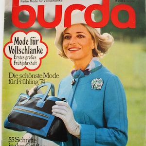 May include: A 1974 Burda magazine cover featuring a person wearing a bright blue jacket, a white hat, and white gloves, holding a black and blue handbag. The cover includes the text burda, Mode für Vollschlanke, and Die schönste Mode für Frühling 74.