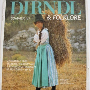 May include: A vintage magazine cover titled DIRNDL & FOLKLORE SOMMER '87 featuring a person wearing a white blouse, a blue and white striped dress, and a solid green apron, carrying a large bundle of hay on their back while wearing a dark hat.
