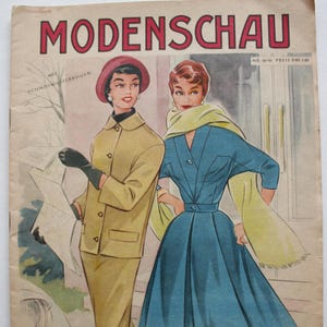 Peut inclure: Une couverture de magazine de mode vintage mettant en scène deux femmes en tenues élégantes. Le magazine s'appelle "Modenschau" et porte le texte "Nr. 34/48 Preis DM 1,80" en haut à droite. La femme de gauche porte une veste et un pantalon beiges, tandis que la femme de droite porte une robe bleue avec une écharpe jaune.