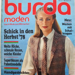 May include: A magazine cover featuring a woman wearing a white shirt with a brown and white plaid waistcoat and a brown tie. The magazine is titled "burda moden" and the text "Schick in den Herbst '78" is visible. The cover also features the text "Neu: Westen mit Schal-kragen".