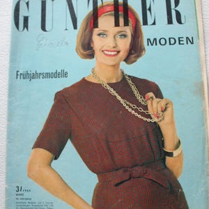 Könnte beinhalten: Vintage Modezeitschrift-Cover mit dem Titel "GÜNTHER MODEN" und dem Text "Frühjahrsmodelle". Es zeigt eine Frau in einem weinroten Kleid mit Schleife und goldener Halskette. Die Frau trägt ein rotes Stirnband. Der Hintergrund ist hellblau.