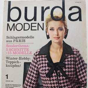 Könnte beinhalten: Ein Magazincover mit einer Frau, die eine pink-schwarze Hahnentrittjacke mit einer schwarzen Schleife trägt. Das Magazin heißt "burda MODEN" und hat den Text "Schlagermodelle aus PARIS" und "Sonderthema: 5 SCHNITTE - 15 MODELLE" auf dem Cover.