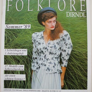 May include: Magazine cover with a woman in a floral blouse and skirt, with the text "FOLKLORE DIRNDL" and "Sommer '89". The background is tall green grass. Additional text includes "1 Schnittbogen und 1 Anleitungsheft" and details about the magazine.