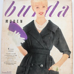 Könnte beinhalten: Ein Vintage-Magazin-Cover der Burda Moden vom Januar 1960 mit einer Person in einem schwarzen, doppelreihigen Mantel mit breitem Kragen, einer mehrreihigen Perlenkette und weißen Handschuhen, die eine violette Clutch und ein Blumen-Corsage hält.