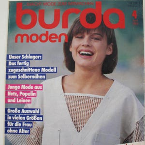 Può includere: Una copertina di rivista vintage con il titolo "Burda Moden" in grandi lettere rosse. La copertina presenta una donna sorridente e vari elementi testuali, tra cui "Schnelle Modelle" e altre frasi legate alla moda. La rivista ha un'estetica retrò.