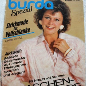 Op de afbeelding: Een vintage magazine cover met een vrouw in een roze trui en grote oorbellen. Het tijdschrift heet "burda Spezial" en bevat Duitse tekst, waaronder "MASCHEN-PARADE" en "Strickmode für Vollschlanke".