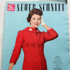 Może przedstawiać: Okładka magazynu w stylu vintage z kobietą w czerwonym, teksturowanym płaszczu z białymi guzikami. Tytuł magazynu to "NEUER SCHNITT" w kolorze czarnym. Tło jest jasnoniebieskie. Z datą listopad 1958.