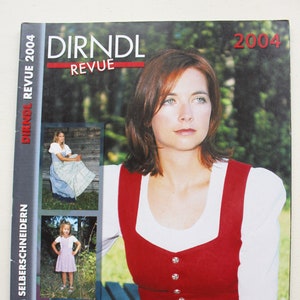 May include: The cover of a "Dirndl Revue 2004" magazine features a woman in a traditional red and white outfit. The magazine includes images of traditional dresses and text in German.