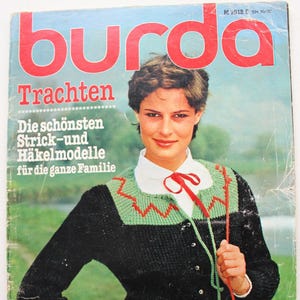 May include: A vintage Burda magazine cover showing a woman in a black knitted cardigan with green and red detailing. The cover text includes "Trachten" and "Die schönsten Strick-und Häkelmodelle für die ganze Familie."