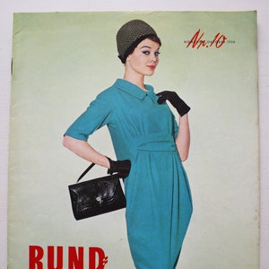 Op de afbeelding: Vintage magazine cover met een vrouw in een turquoise jurk, zwarte handschoenen en een patroonhoed. De cover toont de tekst "RUND SCHAU" in het rood, met Duitse tekst eronder. De vrouw draagt een zwarte handtas.