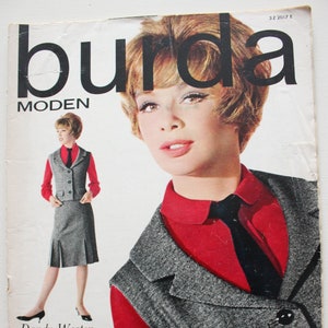 May include: A vintage magazine cover featuring the word "burda" in large, bold letters above the word "MODEN". The cover features a woman wearing a red collared shirt with a black tie and a gray tweed vest. The text on the cover reads "Dandy-Westen und aktuelle Röcke BOUTIQUE-MODE IN SEIDE 1 1963".