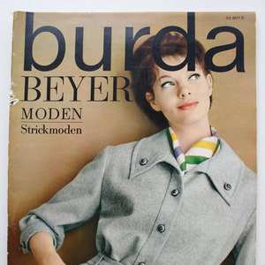 Może przedstawiać: Okładka czasopisma przedstawiająca kobietę w szarej dzianinowej sukience z kolorowym szalem. Czasopismo nosi tytuł "burda BEYER MODEN Strickmoden", a data to październik 1963.