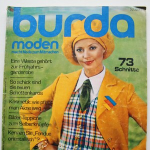 Könnte beinhalten: Ein Vintage-Magazincover mit einer Frau, die eine gelbe Jacke mit einer karierten Weste und einem Barett trägt. Das Magazin heißt "burda moden" und der Covertext lautet "macht Mode zum Mitmachen" und "73 Schnitte".