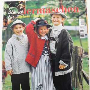 Könnte beinhalten: Ein Magazincover mit drei Kindern, die gestrickte Kleidung tragen. Das Magazin heißt "Blümchenmaschen für Michem Charme" und der Text "Stricken und Nähen in Größe 92-176" ist sichtbar. Das Magazincover zeigt auch den Text "Landhaus-Maschen & Kombimode".