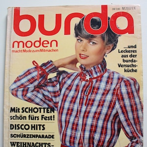 Könnte beinhalten: Ein Vintage Burda Moden Magazin-Cover vom Dezember 1979 mit einer Person in einem rot-weiß-blauen karierten Langarmhemd mit hohem Kragen, einer roten Schleife mit Sternanhänger und einer roten Taillenschärpe über einem blauen Rock.