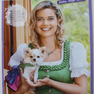 May include: A magazine cover for "DIRNDL Revue" shows a woman in a green and white traditional dress with a small dog. The magazine has a purple border and the text "Trachtenmode zum Selbstschneidern 2019".