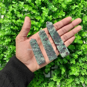 Peut inclure: Trois pointes de pierres précieuses vertes et rouges, également connues sous le nom de rubis en zoïsite, sont présentées dans une main. Les pointes mesurent environ 5 cm de long.