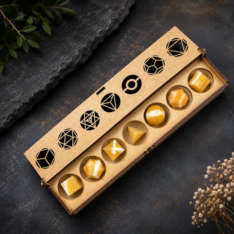 May include: A wooden box with geometric cutouts and containing eight yellow gemstone shapes. The box is open, revealing the gemstones in various shapes, including cubes, spheres, and pyramids. The box is on a dark surface with decorative elements.