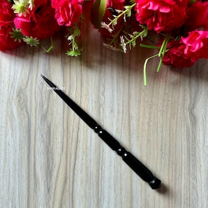 Puede incluir: Un palo de pelo de madera negro con una punta puntiaguda y un extremo redondeado. El palo está sobre una superficie de madera.