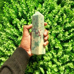 May include: A green and red crystal point with a pointed tip. The crystal has a mottled appearance with green and red swirls.