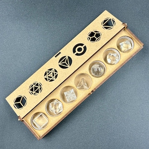 May include: A wooden box with a laser-cut geometric design on the lid, containing clear, faceted crystal shapes. The box is rectangular and has a natural wood finish. The crystals are various geometric forms, including cubes, pyramids, and spheres.