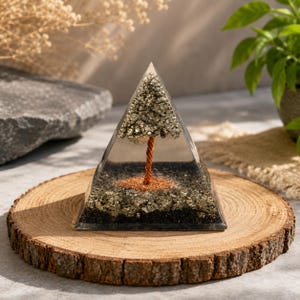 Pode incluir: Uma pirâmide de resina transparente contendo uma escultura de árvore em miniatura com um tronco de fio cor de cobre e folhagem de pedras de pirita douradas, sobre uma base de fragmentos minerais pretos e dourados na resina.
