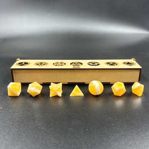 May include: A set of geometric resin dice in various shapes and colors, including cubes, pyramids, and spheres. The dice are yellow and white, and are displayed in a wooden box with decorative cutouts.