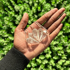 May include: A set of four clear quartz crystal pendulums with silver chains. The pendulums are in the shape of a point and are arranged in a fan shape.