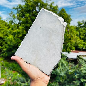 Puede incluir: Una losa de cuarzo blanco translúcido, grande, plana y de forma irregular y dentada. Los bordes de la piedra están recubiertos con un acabado plateado metálico, creando un borde distintivo sobre la superficie cristalina semiopaca.