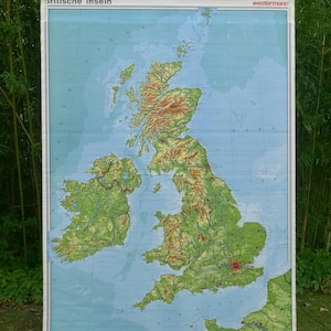 Op de afbeelding: Een grote kaart van de Britse eilanden, met topografische kenmerken in groen, bruin en blauw. De kaart is getiteld "Britische Inseln" en is gemonteerd op een rood omkaderde displaystandaard. De kaart is van westermann.