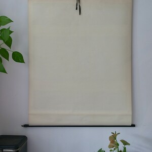 May include: A vintage cream-colored chart hanging on a wall, suspended by a black metal rod and a black ribbon. The chart is rolled at the bottom. The background includes a coffee tin, plants, and a mechanical gear.