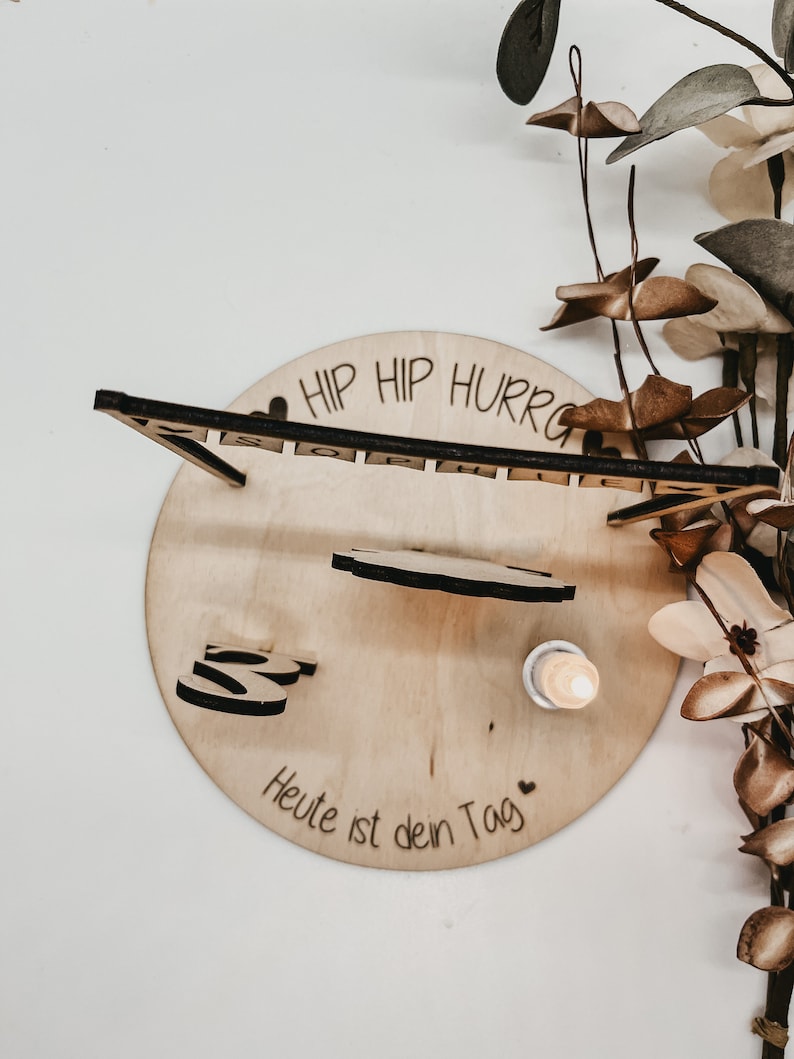 Pu&ograve; includere: Decorazione per compleanno in legno con il testo "Hip Hip Hurray" e "Heute ist dein Tag" (Oggi &egrave; il tuo giorno) in tedesco. La decorazione include una piccola figura di legno e una candela.