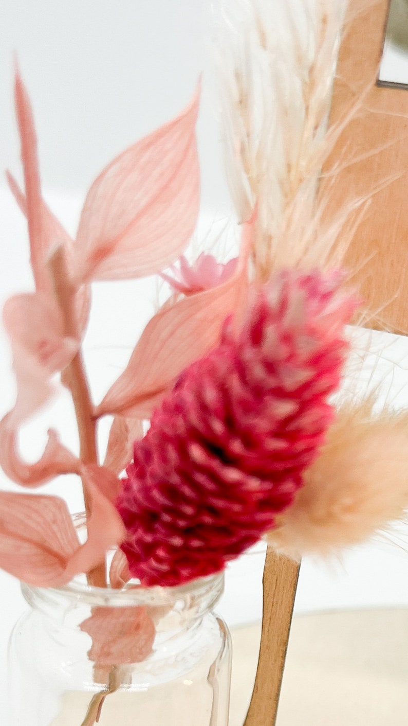 Pu&ograve; includere: Un piccolo vaso di vetro trasparente con un arrangiamento di fiori secchi rosa e rossi. Il vaso &egrave; in vetro trasparente e i fiori sono rosa e rossi.