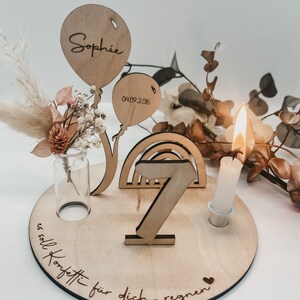 Pu&ograve; includere: Decorazione di compleanno in legno con un arcobaleno, un numero 7, un portacandele e due palloncini. I palloncini sono personalizzati con il nome "Sophie" e la data "04.09.2016". La base della decorazione ha il testo "es soll Konfetti f&uuml;r dich regnen" inciso.